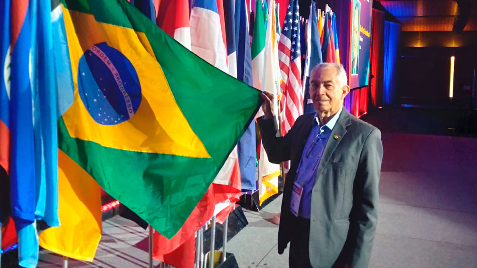 Presidente do Sicoob Credileste, Ladir Firmino de Oliveira, ao lado da bandeira do Brasil.
