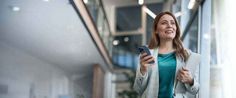 Mulher sorrindo enquanto olha o celular em um escritório