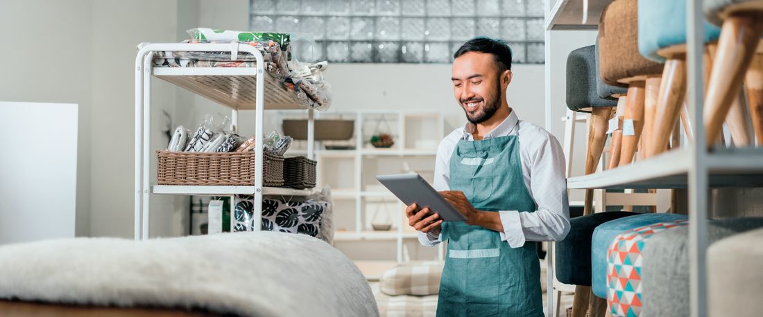 Comerciante de avental sorrindo enquanto usa um tablet em sua loja